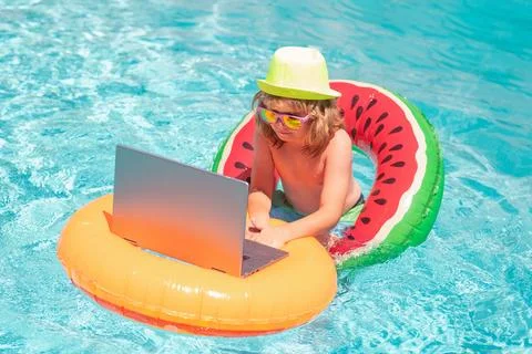 Freelance work concept. Kid boy relaxing in the pool, using laptop computer in 스톡 사진