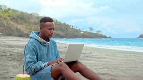 Freelance work ocean beach. Black person use laptop macbook African american man Stock Footage 246407315