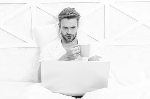 Freelancer in bed. Millennial man work on laptop at home. Man lying in bed and Stock Photos