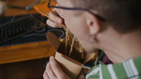 Freelancer Coding on Computer and Eating Noodles with Chopsticks at Home Stock Footage 334804102
