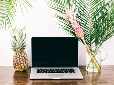 Freelancer desktop whith computer,  palm branches and decorative pink pineapp Stock Photos