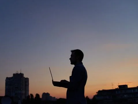 Freelancer developer in silhouette using laptop outdoor at sunset 库存照片