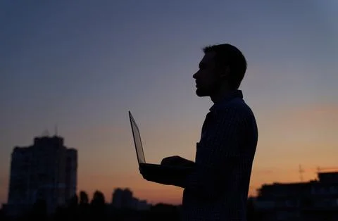 Freelancer developer in silhouette using laptop outdoor at sunset, working hard Stock Photos