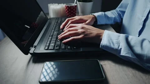 Freelancer developer student in shirt is typing on a laptop with a phone next 스톡 동영상 344915377