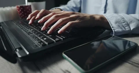Freelancer developer student in shirt is typing on a laptop with a phone next 動画素材 344915390
