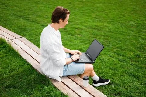Freelancer doing remote work on a laptop outdoors. Man sitting on a wooden .. Stock-Fotos
