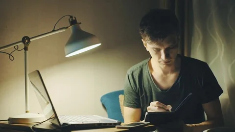 Freelancer dressed in a T-shirt working at home on a laptop computer at evening Stock Footage 78766755