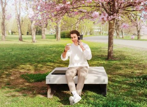 A freelancer enjoys remote work in a spring park under pink blossoms. The m.. 스톡 사진