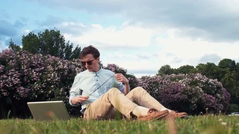 Freelancer having video call at laptop sitting on grass at city park. Summer day Stock-Footage 77168050