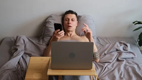 Freelancer lying in bed recording voice message on phone while making Stock Footage 314515454