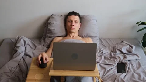 Freelancer lying in bed working intensively on laptop feeling tired and Stock Footage 314893145