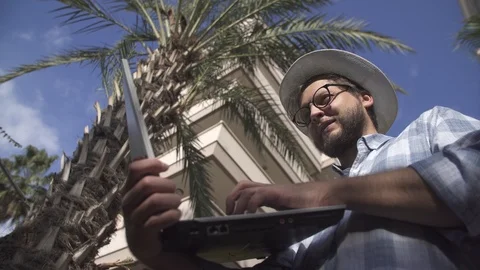 Freelancer man with laptop working on the beach under palm trees Stock Footage 121343798