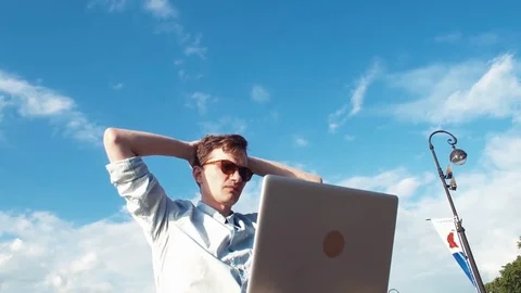 Freelancer man using laptop sitting on bench near seafront. Celebrating success. Stock-Footage 77167664