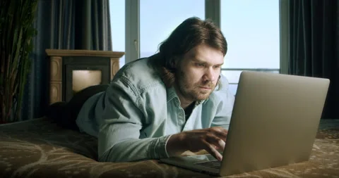 Freelancer man working at home with laptop lying on bed. Copyrighter, content Stock Footage 252153519