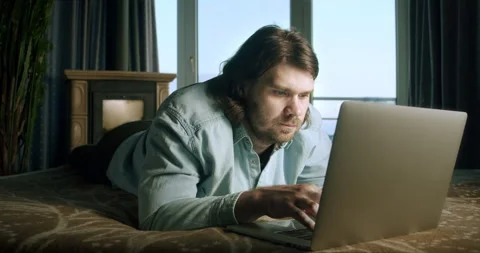 Freelancer man working at home office with laptop lying on bed. Chatting online Stock Footage 252154028