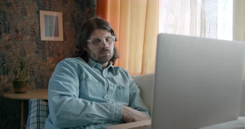 Freelancer, pensive man working at home with laptop. Watching media content Stock Footage 245806022