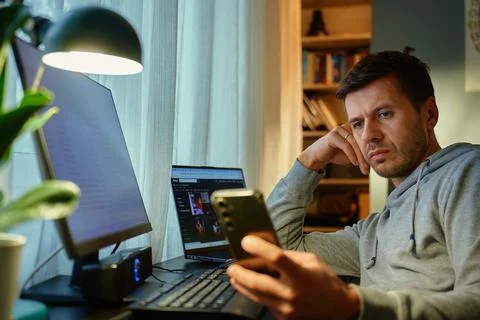 Freelancer procrastinating at home office, scrolling phone instead of working Stock Photos
