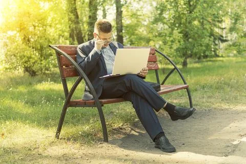 Freelancer programmer sitting at laptop on a bench in Park outdoors. business 写真素材