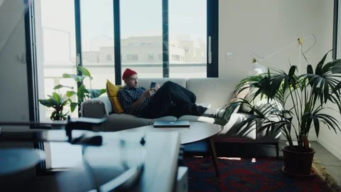 Freelancer relaxing on sofa using smartphone in modern apartment Stock Footage 312999294