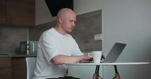 A freelancer sits alone in his kitchen and works using a laptop Stock Footage 302901448