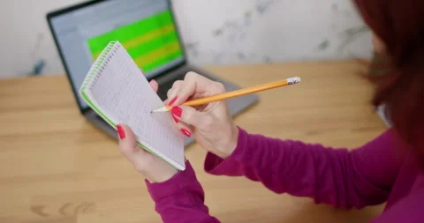 Freelancer studies chart on computer writing down data in small pad Vidéo 294697492