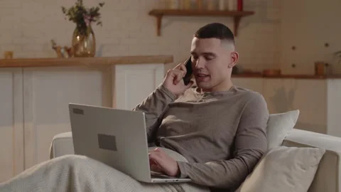 A freelancer is talking to an employer on the phone while lying on the couch Stock Footage 235784036