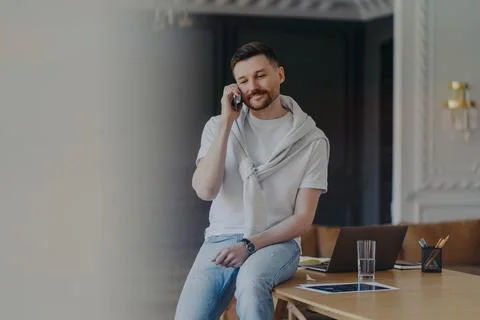 Freelancer talking on phone while sitting on work desk at home office Stock Photos