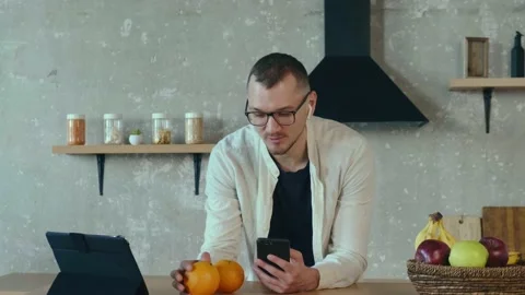 Freelancer talking on smartphone and using tablet in the kitchen. Mobile Stock Footage 176589365