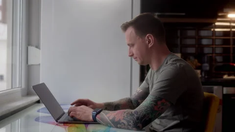 Freelancer in tattoo work at laptop while sitting in background of kitchen Stock Footage 232746934