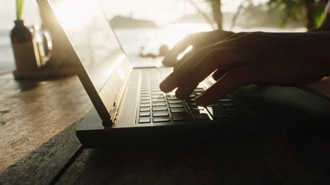 Freelancer types on laptop at sunset beach cafe, finishing project. Warm light Stock Footage 281238731