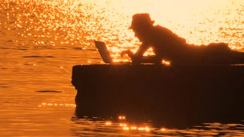 Freelancer typing on laptop over sunset reflecting in sea water. Male, blogger Stock Footage 139772572