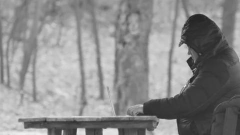 Freelancer typing on a laptop at a table in the forest, side view, in black 库存影片 174842047