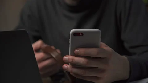 Freelancer typing a message on the phone late at night at his desk at home Stock Footage 172574989