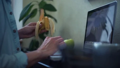 Freelancer using laptop eating banana at home. Young man working out off office Stock Footage 82932810