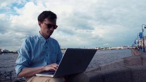 Freelancer using laptop sitting on bench near seafront. Summer day Stock Footage 77167408