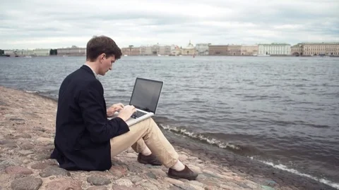 Freelancer using laptop sitting on bench near seafront. Summer day Stock Footage 80009099