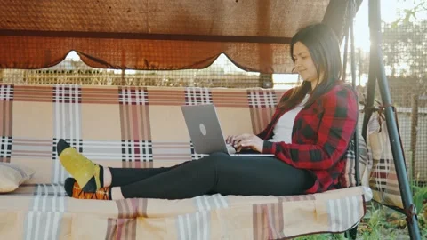 Freelancer using a laptop while sitting on a cozy swing in his backyard Stock Footage 244647959