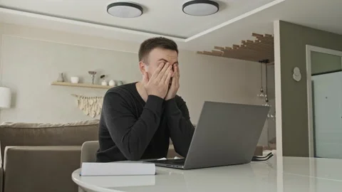 Freelancer using laptop working from home in internet. Tired guy rubs his face Stock Footage 133782450