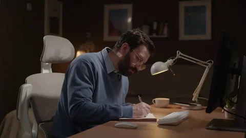 Freelancer at work. Male remote worker takes notes in diary and looks at Stock-Footage 337646944