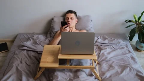 Freelancer working in bed multitasking with laptop and phone Stock Footage 314513669