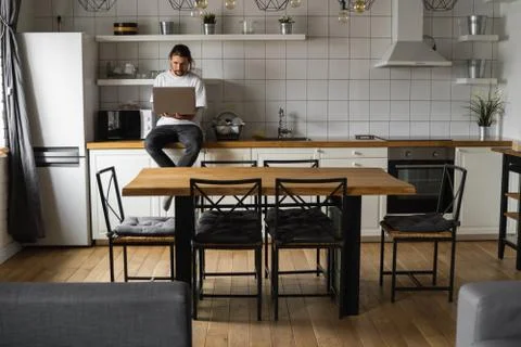 Freelancer working from home sitting on a kitchen worktop and using laptop Stock Photos