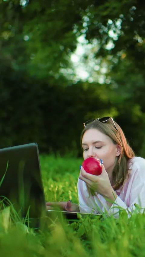 Freelancer Working Outdoors on Laptop While Eating Apple in Lush Green Stock Footage 317583247