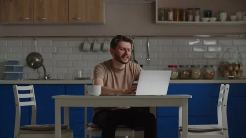 A freelancer works remotely on a laptop while sitting in the kitchen in his Stock Footage 239001518