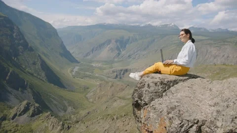 Freelancer works remotely in mountains sitting on edge of cliff overlooking Stock Footage 155703401