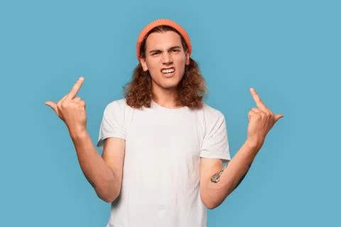 Freestyle. Curly-haired guy wearing hat standing isolated on blue showing middle Stock Photos