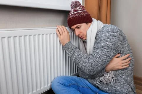 Freezing man in hat and scarf hugging cold radiator to warm up during winte.. 스톡 사진