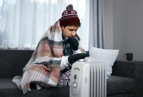 Freezing man warming his hands over a radiator at home. This highlights a s.. Stock Photos