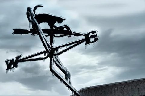 Freezing rain on wind direction indicator against grey sky Stock Photos