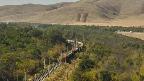 Freight long cargo train carries lorry carriages by arid hilly landscape. Railwa Vidéo 263972181