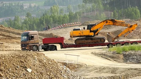 A freight tractor with a trailer conveys the excavator along a sandy dusty road Stock Footage